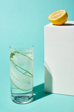 turkuaz arka plan üzerinde limon yarısına yakın saf su ve salatalık dilimleri ile şeffaf cam