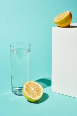 turkuaz arka plan üzerinde limon yarıya yakın saf su ile şeffaf cam
