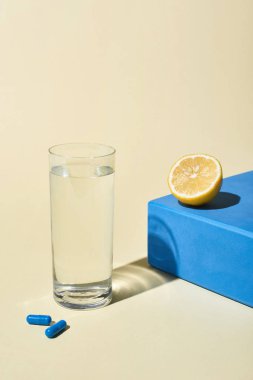 bej arka planda mavi küp üzerinde su, mavi hap ve limon yarısı cam