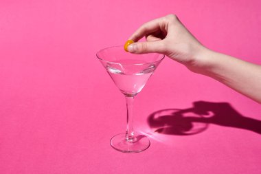 pembe arka plan üzerinde kokteyl ile cam zeytin koyarak kadın kırpılmış görünümü