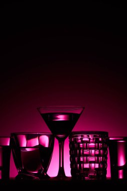 transparent glasses with liquid on dark background with pink illumination clipart