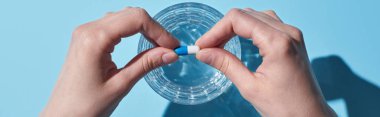partial view of woman putting pill in glass with water on blue background, panoramic shot clipart