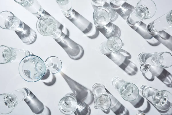 top view of transparent glasses with clear water on white background with shadows