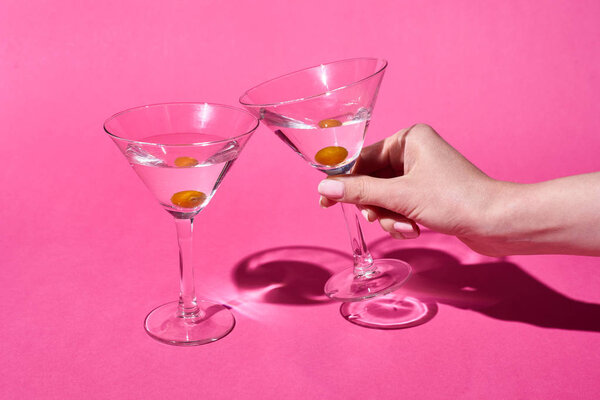 обрезанный вид женщины, держащей стакан коктейля на розовом фоне
