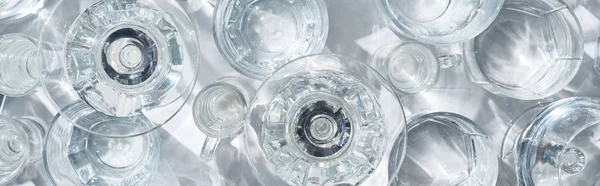 top view of transparent glasses with pure water on white background with shadows, panoramic shot