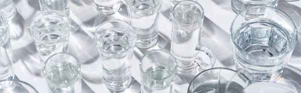 close up view of transparent glasses with water on white background with shadows, panoramic shot