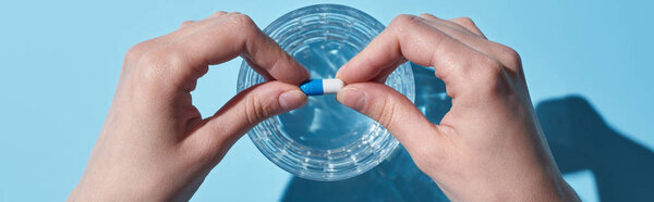 partial view of woman putting pill in glass with water on blue background, panoramic shot