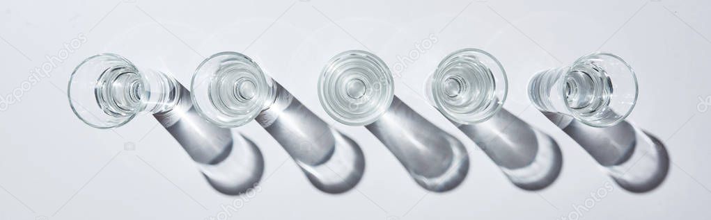 top view of transparent glasses with water in row on white background with shadows, panoramic shot