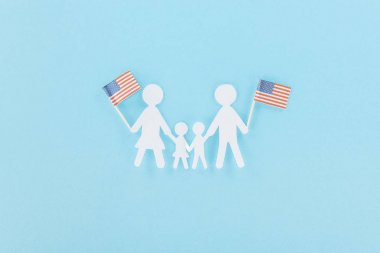 mavi arka plan üzerinde ahşap çubuklar üzerinde dekoratif Amerikan bayrakları tutan kağıt kesilmiş aile üst görünümü