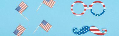 panoramic shot of glasses and mustache made of stars and stripes near decorative american flags on wooden sticks on blue background clipart