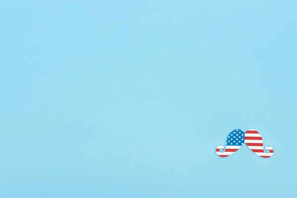 top view of mustache made of american flag on blue background with copy space