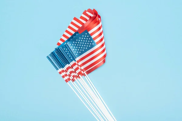 top view of american flags on sticks stacked on blue background