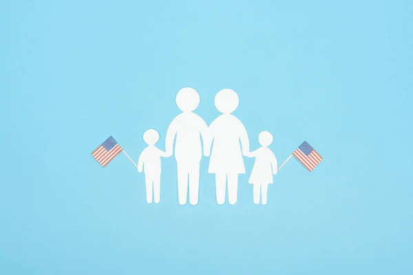 top view of white paper cut family holding decorative american flags on wooden sticks on blue background