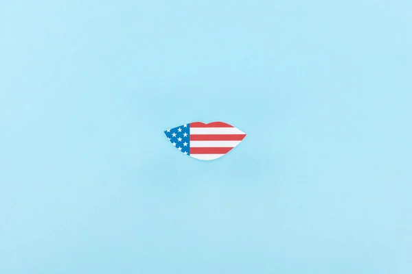 top view of paper cut lips mustache made of american flag on blue background 
