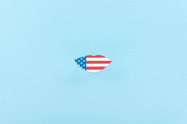 top view of paper cut lips mustache made of american flag on blue background 