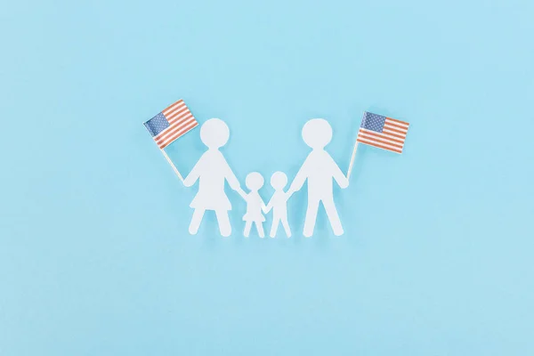 top view of  paper cut family holding decorative american flags on wooden sticks on blue background