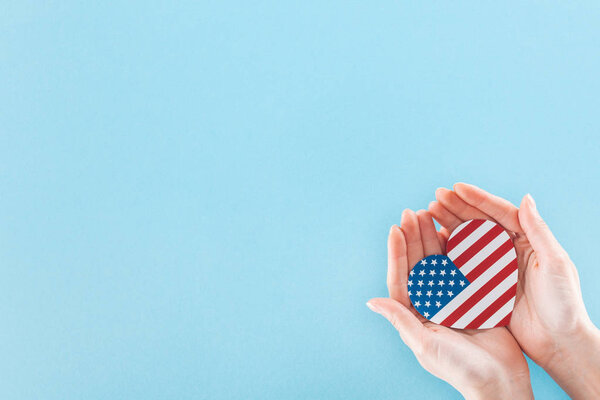 cropped view of woman holding heart made of national american flag on blue background with copy space