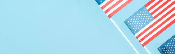 panoramic shot of american flags on sticks on blue background with copy space