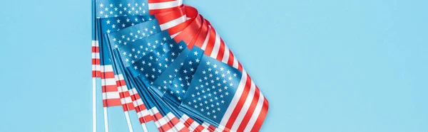 panoramic shot of glossy american flags on sticks on blue background