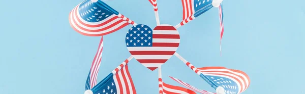 top view of american flags in circle with heart on blue background, panoramic shot
