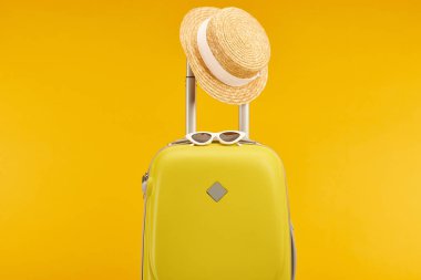 yellow colorful travel bag with sunglasses and straw hat on handle isolated on yellow clipart
