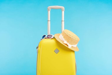 sarı renkli seyahat çantası, hasır şapka ve güneş gözlüğü mavi izole edilmiş.