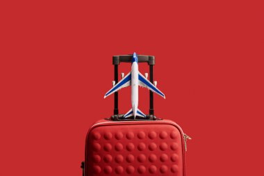 red colorful textured travel bag with plane model isolated on red  clipart