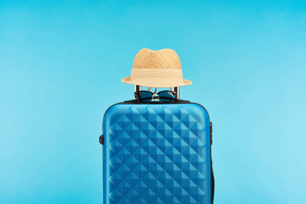 blue colorful travel bag with sunglasses and straw hat isolated on blue
