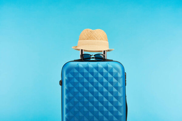 blue colorful travel bag with handle, sunglasses and straw hat isolated on blue 