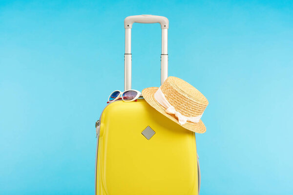 yellow colorful travel bag with straw hat and sunglasses isolated on blue