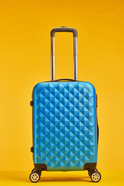 blue travel bag with handle on wheels isolated on orange