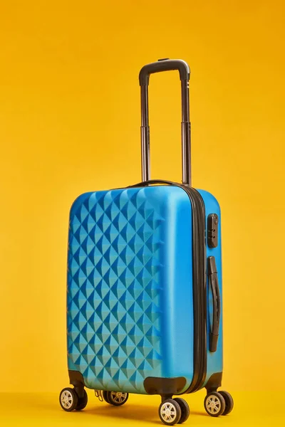 blue plastic travel bag with handle on wheels isolated on orange