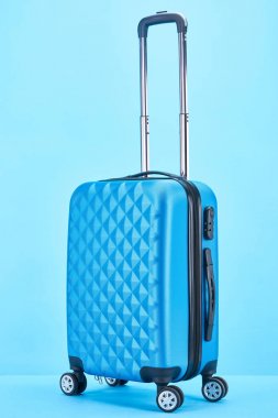 blue colorful suitcase with handle on wheels on blue background clipart