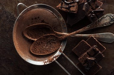 Top view of dirty strainer, vintage spoons and pieces of chocolate bar on rust metal background clipart
