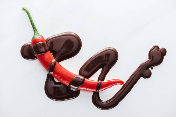 Top view chili with spilled melted dark chocolate on white background