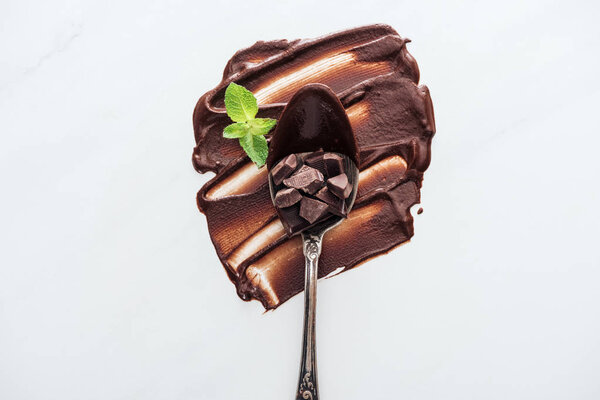 Top view of vintage spoon with pieces of chocolate bar and fresh mint 
