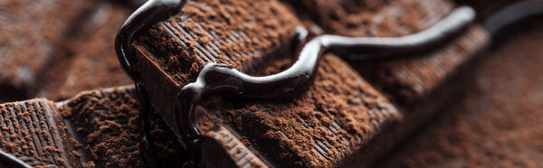 Panoramic shot of pieces of dark chocolate bar with liquid chocolate 