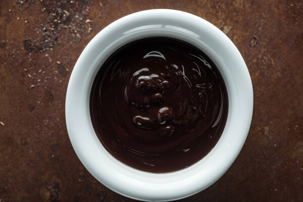 Вид сверху чаши с расплавленным шоколадом на ржавом металлическом фоне

