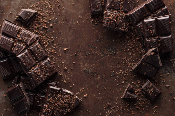 Top view of pieces of chocolate bar with chocolate chips on rust metal background 