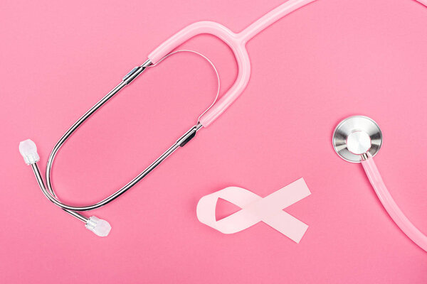 top view of stethoscope and pink breast cancer ribbon on pink background