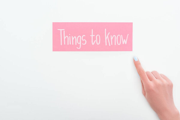 partial view of woman pointing with finger at pink card with things to know lettering on white background