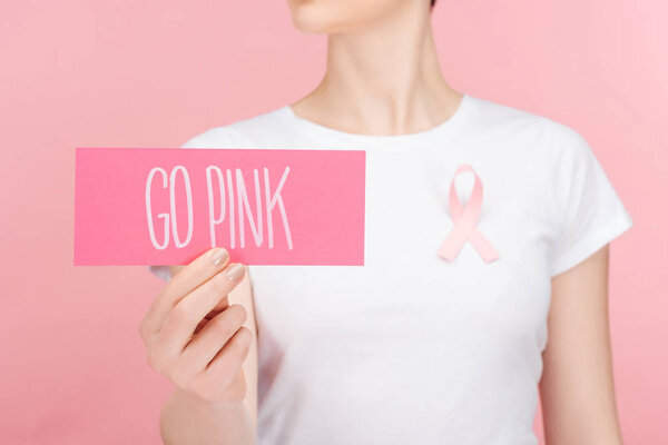 selective focus of woman with pink breast cancer sign holding pink card with go pink lettering isolated on pink