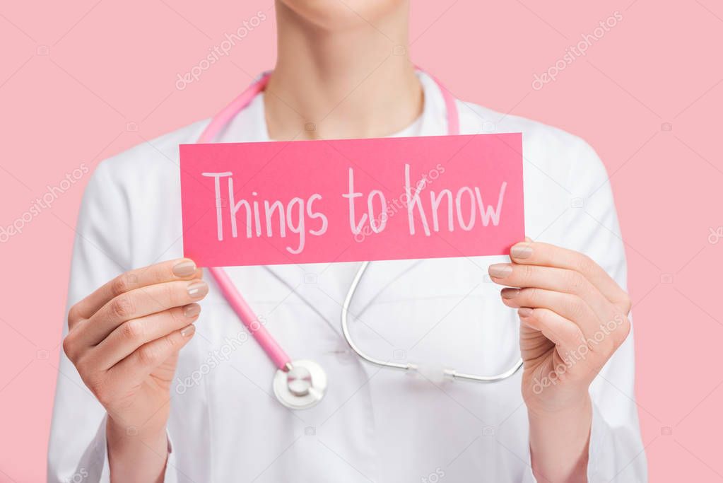 cropped view of doctor in white coat and stethoscope holding card with things to know lettering isolated on pink