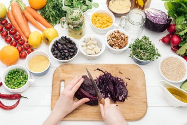 cropped view of woman cutting red cabbage on wooden chopping board clipart