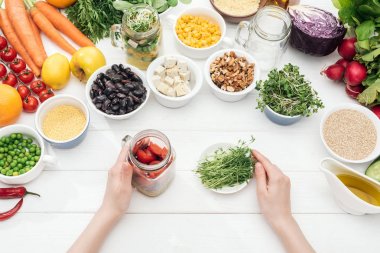 ahşap beyaz masada otlar ile salata ve tabak ile cam kavanoz tutan kadın kırpılmış görünümü