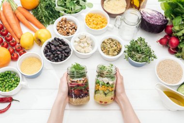 cropped view of woman holding glass jars with fresh salad on wooden white table  clipart