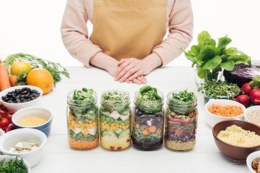beyaz izole ahşap masa üzerinde salata ile cam kavanoz yanında duran önlük kadın kısmi görünümü