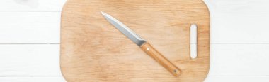panoramic shot of wooden chopping board with knife on white table clipart