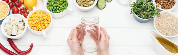 cropped view of woman holding empty glass jar on wooden white table, panoramic shot