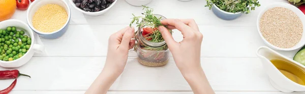 木製の白いテーブルの上にサラダと瓶に緑の芽を追加する女性のトリミングビュー パノラマショット — ストック写真